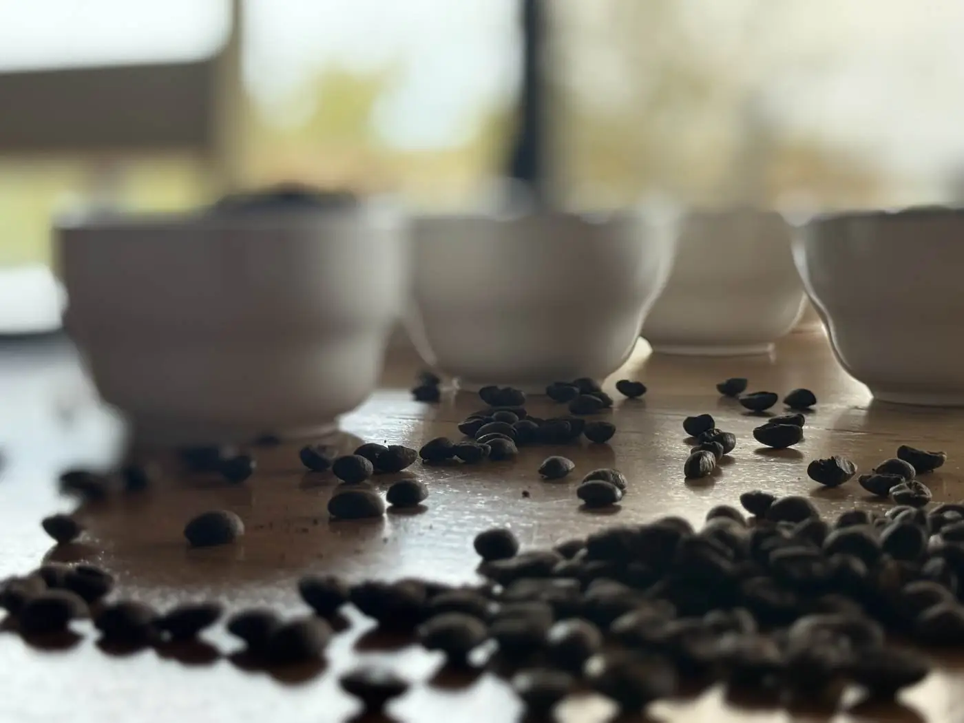 Roasted whole beans scattered in front of white cupping bowls