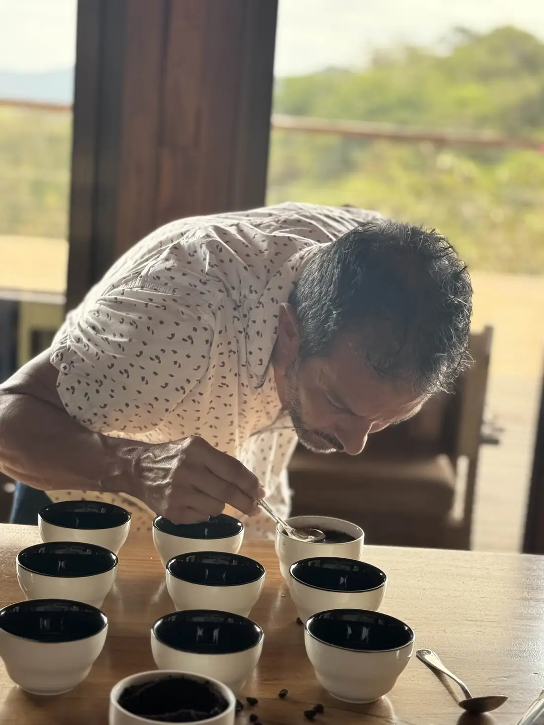 A taster leans over a row of cupping bowls with a spoon, smelling and tasting each cup