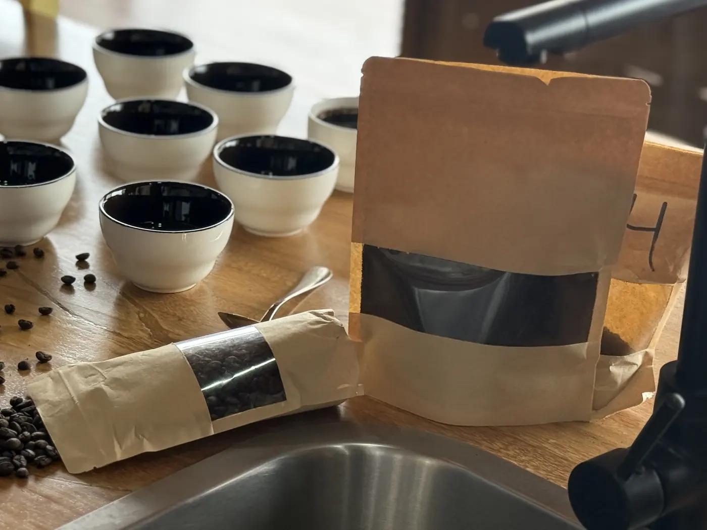 Kraft coffee pouches with a window beside roasted beans and cupping bowls